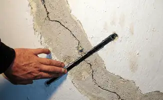 A wall with a large crack is being inspected by a professional in Bloomington, IN